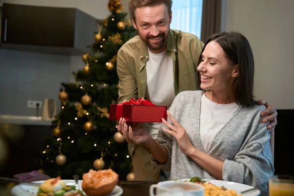 Happy man giving present to beautiful woman while having festive New Year dinner celebrating holidays together
