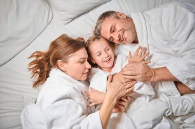 Anne, baba ve kızının otel odasında yatıp dinlendiği mutlu beyaz bir aile manzarası. Dinlenme, tatil ve seyahat kavramı. Aile ilişkisi ve birlikte zaman geçirmek.