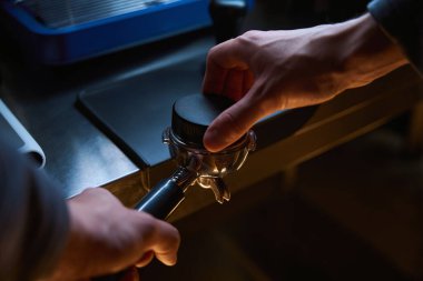 Barista kahvehanedeki portafilter içine kahve basmak için kurcalayıcı kullanıyor.