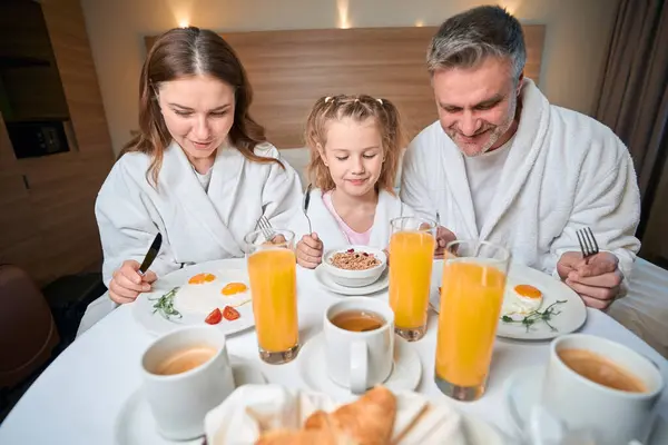 娘のヨーロッパの家族は ホテルの部屋のテーブルでベッドで朝食をとっています 旅行のコンセプト 家族関係のアイデアと一緒に時間を過ごす — ストック写真