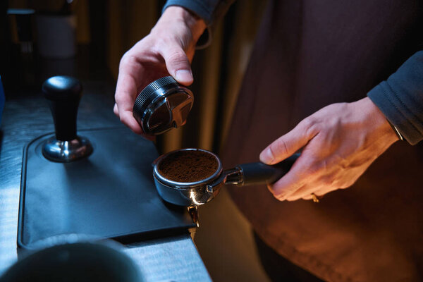 Бариста выравнивает молотый кофе в портативном фильтре в кафе