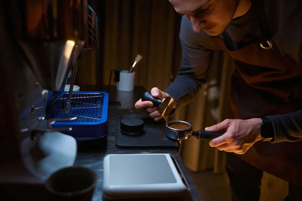 Barista holding portafilter with grinded coffee and tampering working in coffee shop