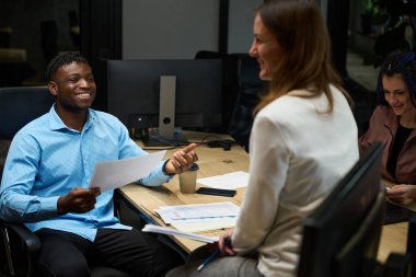 Çok ırklı pazarlamacılardan oluşan neşeli bir ekip birlikte çalışan uzay ofisinde toplantı düzenliyor, verileri analiz ediyor ve gelecek siparişleri ve sevkiyatları tahmin ederken eğleniyor.