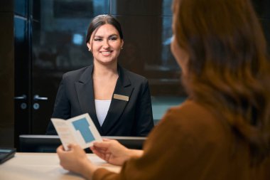 Pasaportlu kısmi kadın ve gülümseyen Avrupalı kadın resepsiyonist otel lobisindeki resepsiyonda birbirlerine bakıyorlar. Dinlenme, tatil ve seyahat kavramı