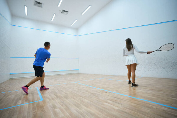 Motivated woman athlete refines squash hitting techniques under man instructors guidance on indoor court