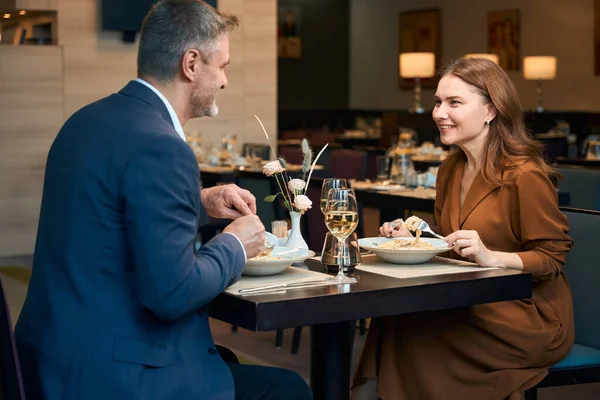 大人の笑顔の白人カップルはパスタを食べて ホテルのレストランでお互いを見ています ロマンチックな日付とイベントのコンセプト — ストック写真