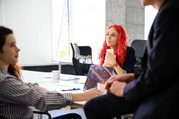Woman office worker with red hair dreaming about big salary and vacations sitting at workplace, dont care to other colleagues in office