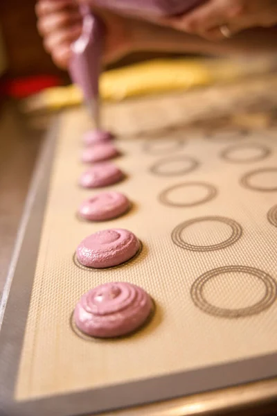 Cropped photo of confectioner hands squeezing macaron batter from piping bag onto silicone baking mat