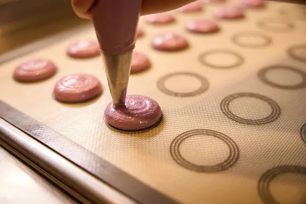 Closeup of hand squeezing macaron batter from pastry bag onto silicone baking mat
