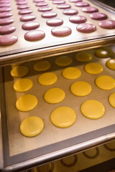 Rows of pink and yellow macarons on silicone mats on sheet pans