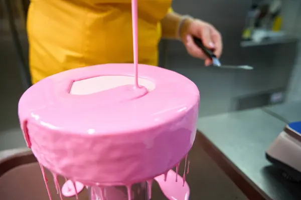 Cropped photo of pastry cook in uniform coating cake with pink icing