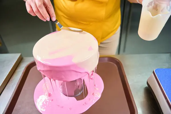 Cropped photo of pastry cook spreading layer of icing on cake with spatula