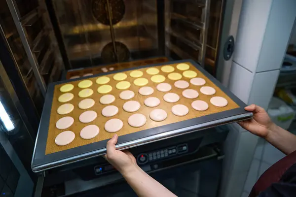 Cropped photo of baker placing sheet pan with with macarons into combi-steam oven