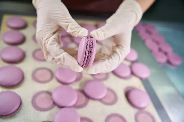 Closeup of hands in disposable gloves assembling macaron shells together over baking mat on worktop