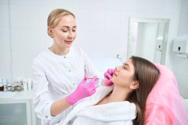 Profesyonel kozmetik uzmanı elinde şırıngayla çenesine iğne yapıyor. Güzellik salonunda prosedür