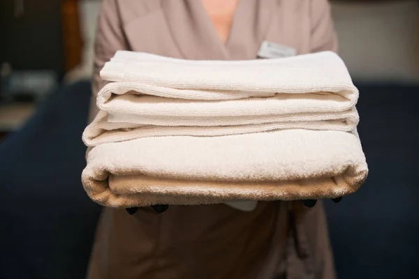 Cropped photo of hotel worker in gloves holding stack of clean white terry towels in hands