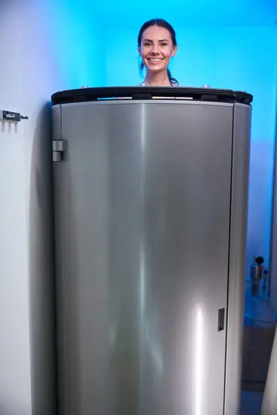 stock image Smiling female standing in cryosauna and ready for procedure in beauty salon