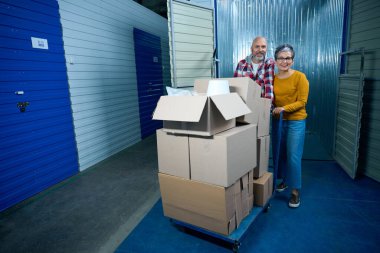 Mülk deposunun koridorundaki karton kutularda iki kişi bir şeyler taşır.