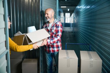 Yaşlı adam bir kutuda paketlenmiş şeyleri süveterli bir kadına verir..