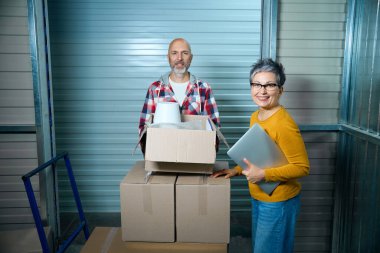 İki kişi eşyalarını taşırken kameraya bakar.