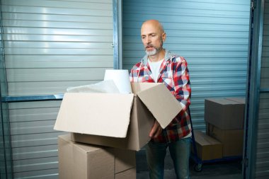 Yaşlı adam hareket ederken yanında bir şeyler taşıyan bir karton kutu tutuyor.