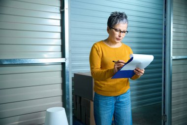 Yetişkin kadın depoda konteynır kiralama belgelerine giriş yapıyor.