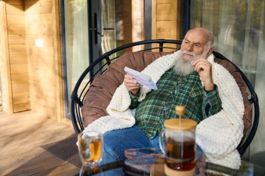 Yaşlı adam hastalıktan muzdarip, elinde bir ilaç kutusu ve bir hap var.