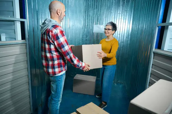 Lady with a short haircut and glasses gives a box of things to a bald man