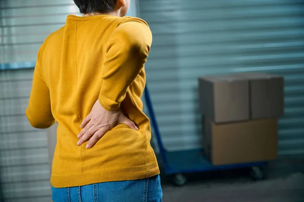 Woman holding her sore back while in storage warehouse for things in boxes