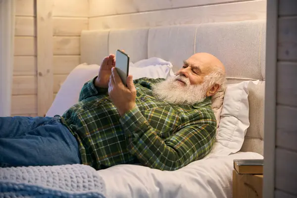 Old man was tired and lay down to rest on a cozy bed, he had a mobile phone in his hands