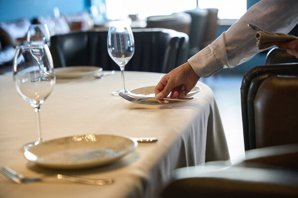 Waitress in a restaurant lays out cutlery, there is a white tablecloth on the table