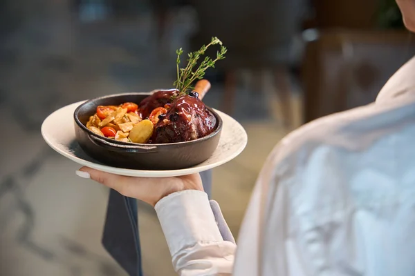 Waitress serves meat with vegetables in a serving pan, traditional serving is used