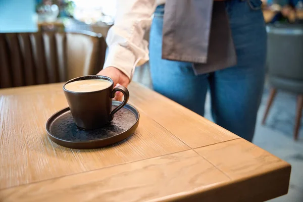 Waiter serves coffee for one person, in a cappuccino cup