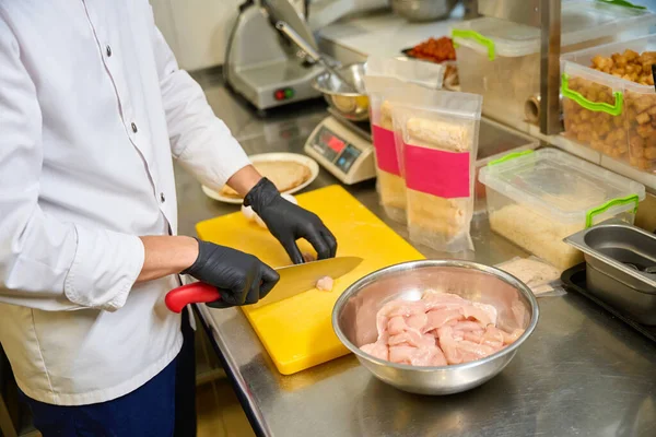 Kitchen staff cuts chicken fillet on a cutting board, quality products are used