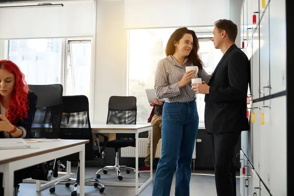 Male and female colleagues talking to each other and laughing during coffee break, mutual sympathy, relationships at work and in the team, coworking space
