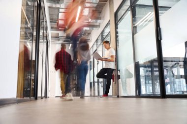 Ofis binasının duvarına yaslanan ve sunumunu dizüstü bilgisayarla bitiren, iş görüşmesine hazırlanan, koridorda bekleyen insanlar.