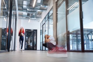 Beyaz tişörtlü genç adam ofis salonunda kıçının üzerinde oturuyor ve başını ellerle örtüyor, işten atılmayla başa çıkamıyor, önemli bir projeden kalıyor, arkadaşlarıyla iş toplantısını kaçırıyor.