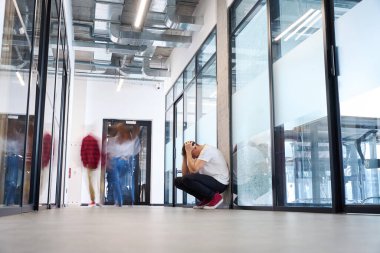Beyaz tişörtlü yorgun bir adam iş merkezinin koridorunda el ele tutuşarak oturuyor, iş görüşmesinde başarısız oluyor, önemli arkadaşlarla buluşmayı unutuyor.