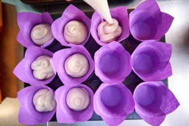 Hamur hamurunun hamur torbasından sıkıştırılıp kek tepsisindeki kağıt kek kalıplarına sıkıştırıldığının en üst görüntüsü