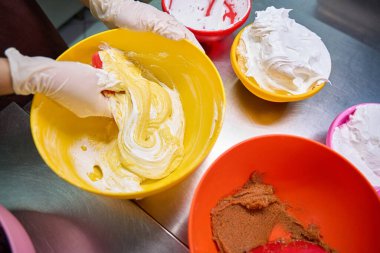 Makaron hamurunu kasede silikon kazıyıcı ile katlayan tek kullanımlık eldivenli pasta şefinin kesilmiş fotoğrafı.