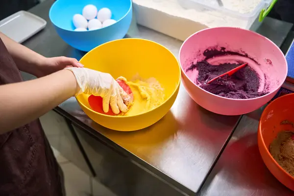 Cropped photo of pastry cook folding macaron batter in bowl with silicone spatula
