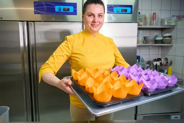 Smiling female pastry chef holding tray with disposable paper cupcake liners filled with batter