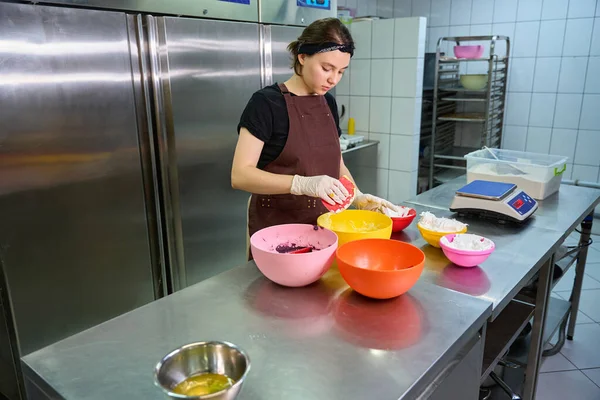 Serious pastry chef with silicone dough scraper in hand looking at macaron batter in bowl