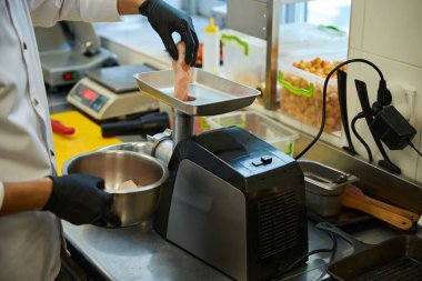 Aşçı et öğütücüsünde et öğütür, adam koruyucu eldiven giyerek çalışır.