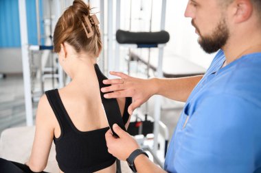 Sıhhiye, bir hastanın arkasına siyah bant yapıştırır. Rahat siyah elbiseli bir kadın.