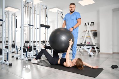 Genç bir kadın spor salonunda antrenör gözetiminde spor yapıyor.