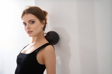 Kadın özel bir aletle duvara karşı egzersiz yapıyor, rahat siyah elbiseli bir kadın.