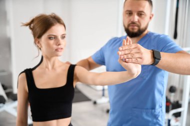 Rehabilitasyon merkezindeki eğitmen genç bir hastayla çalışıyor. Kadın vücuduna bant yapıştırılmış.