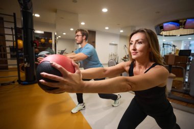 İnsanlar bir topla egzersiz yapıyorlar, modern bir spor salonundalar.