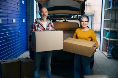 Yetişkin insanlar ellerinde karton kutularla kameraya bakıyorlar.